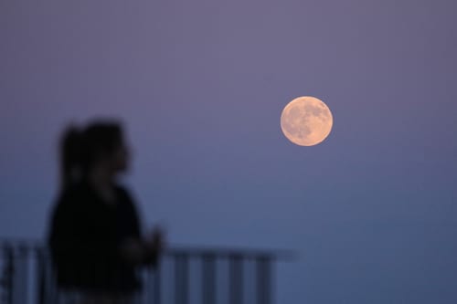A person watches as the full moon rises above the Tagus river hours before a lunar eclipse in Lisbon, Thursday, Aug. 27, 2026. (AP Photo/Armando Franca)