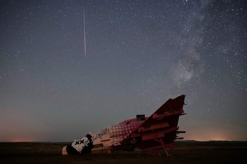 A meteor streaks above a destroyed aircraft used for training purposes in the Negev Desert, Israel, Aug. 13, 2026. (Image Source: AP/Ohad Zwigenberg)