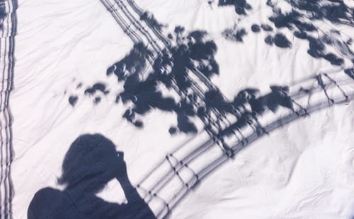 Silhouette of woman photographing shadows of sun crescents cast on a white sheet during the solar eclipse totality in Evansville, IN, USA