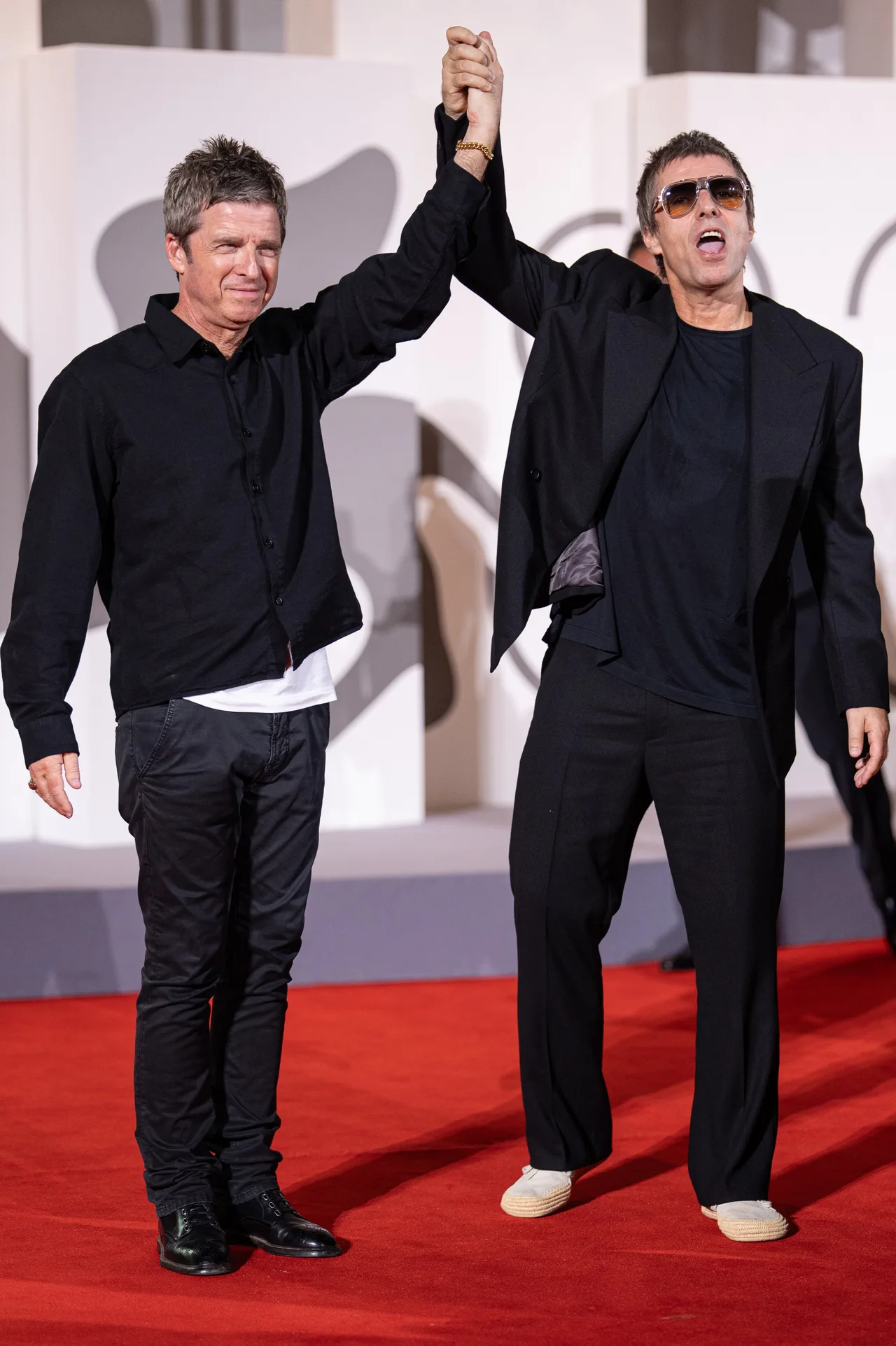 Liam and Noel Gallagher beam as they lock hands in the air
