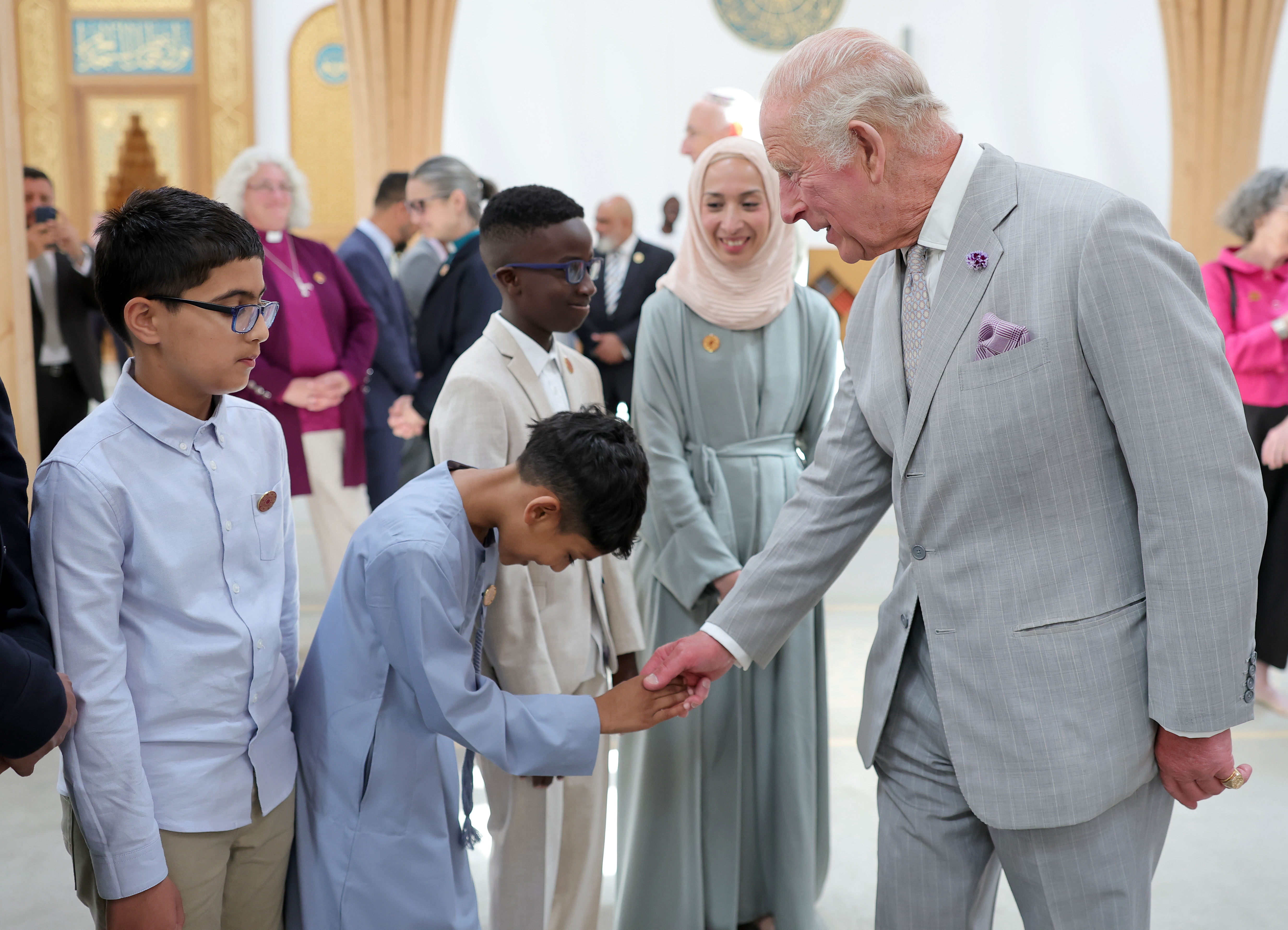 CAMBRIDGE, ENGLAND - JULY 20: King Charles III shakes hands with a young person in the prayer hall during his visit to Cambridge Central Mosque on July 20, 2026 in Cambridge, England. Europe’s first Eco-Mosque, it's notable for its architectural quality, environmental leadership and role as a place of worship and community engagement. (Image source: Getty Images | Photo by Chris Jackson)