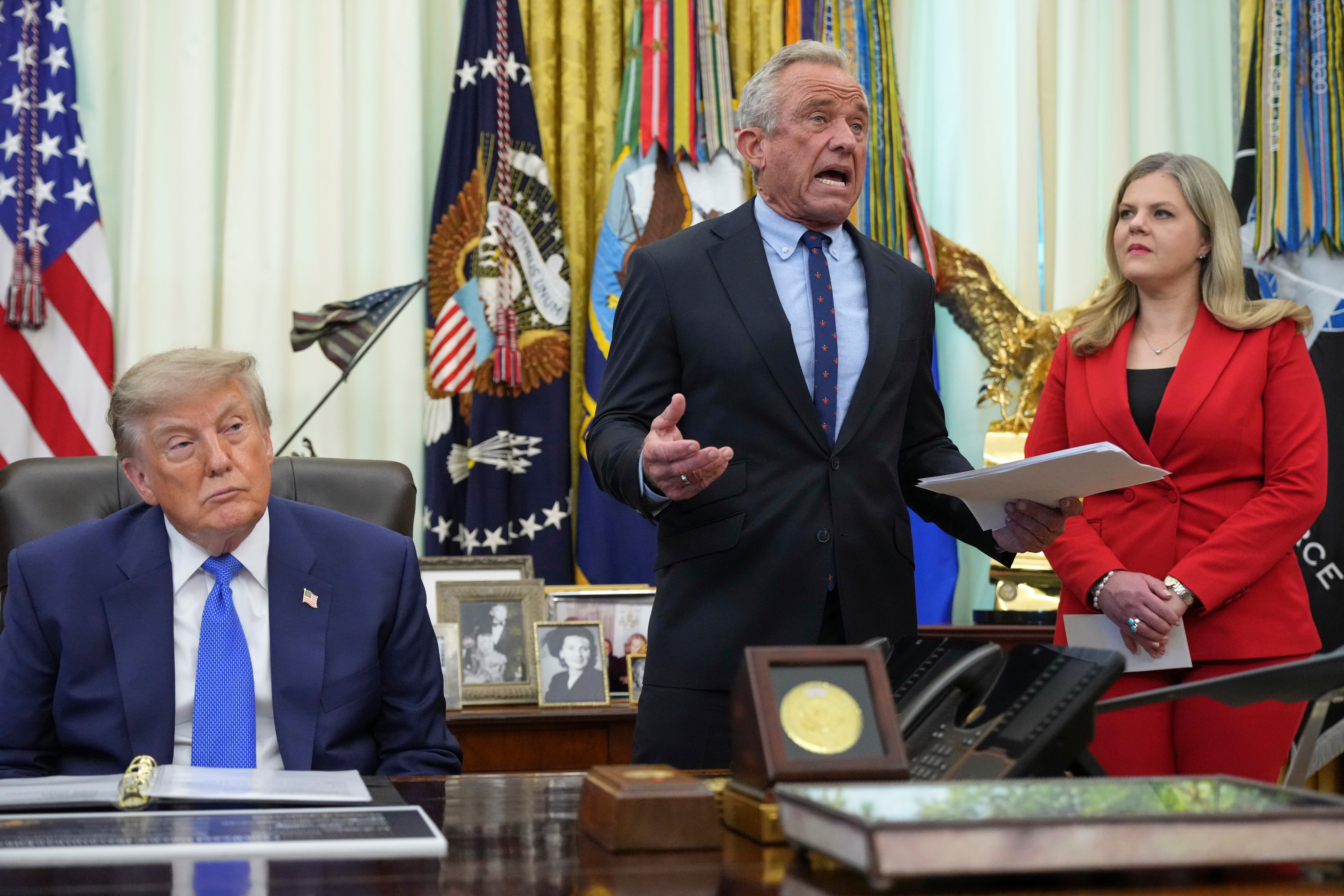 Health and Human Services Secretary Robert F. Kennedy Jr. speaks as President Donald Trump, left, and Heidi Overton, deputy director of the White House Domestic Policy Council, listen during a meeting to sign an executive order about vaccines, Monday, Aug. 10, 2026, in the Oval Office of the White House in Washington. (AP Photo/Jacquelyn Martin)