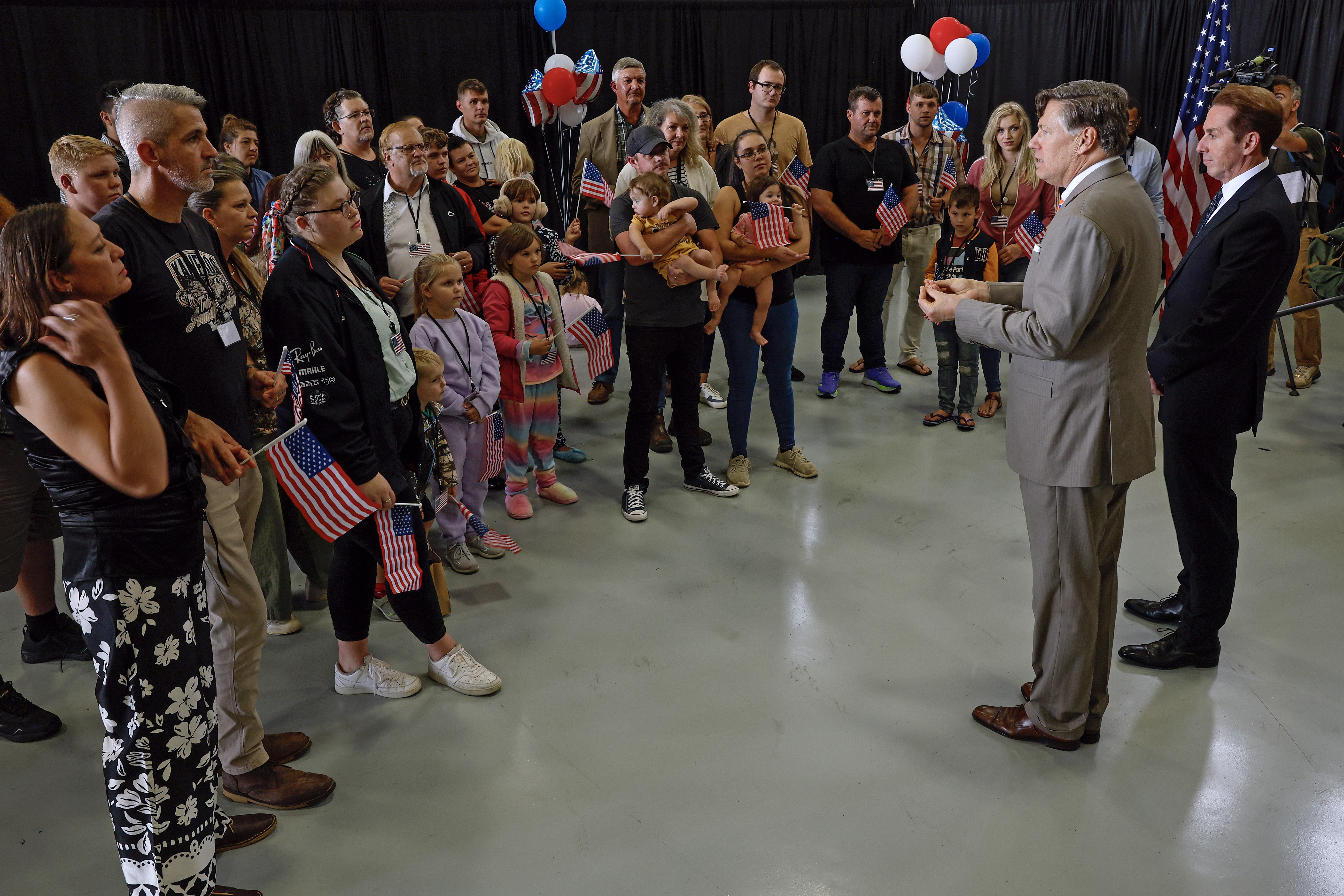 DULLES, VIRGINIA - MAY 12: Newly arrived South Africans listen to U.S. Deputy Secretary of State Christopher Landau and Homeland Security Deputy Secretary Troy Edgar (R) deliver welcome statements in a hangar at Atlantic Aviation Dulles near Washington Dulles International Airport on May 12, 2025 in Dulles, Virginia. About 80 white South Africans, also called Afrikaners, accepted an invitation from the Trump Administration to come to the United States as refugees, fleeing what they say is job discrimination and racial violence in their home country. Trump has halted virtually all refugee admissions for people fleeing famine and war but has created an expedited path into the U.S. for Afrikaners, descendants of white Europeans who created and led the brutal apartheid regime in South Africa from 1948 to 1994. (Photo by Chip Somodevilla/Getty Images)