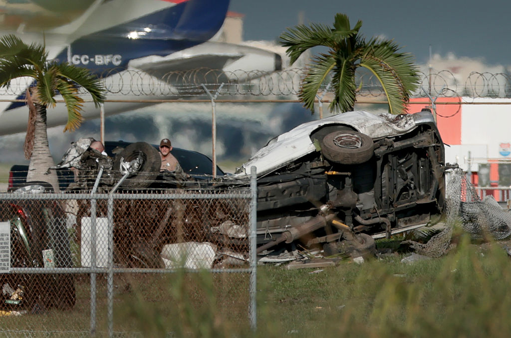 MIAMI, FLORIDA - SEPTEMBER 06: Investigators walk near damaged vehicles at Miami International Airport on September 06, 2026 in Miami, Florida. The vehicles were damaged when an Amazon cargo plane crashed, with five people confirmed killed during the crash. According to the Federal Aviation Administration, Prime Air Flight 7598 overran the runway while landing around 2 p.m. after departing from Luis Muñoz Marín International Airport in San Juan, Puerto Rico. (Photo by Joe Raedle/Getty Images)