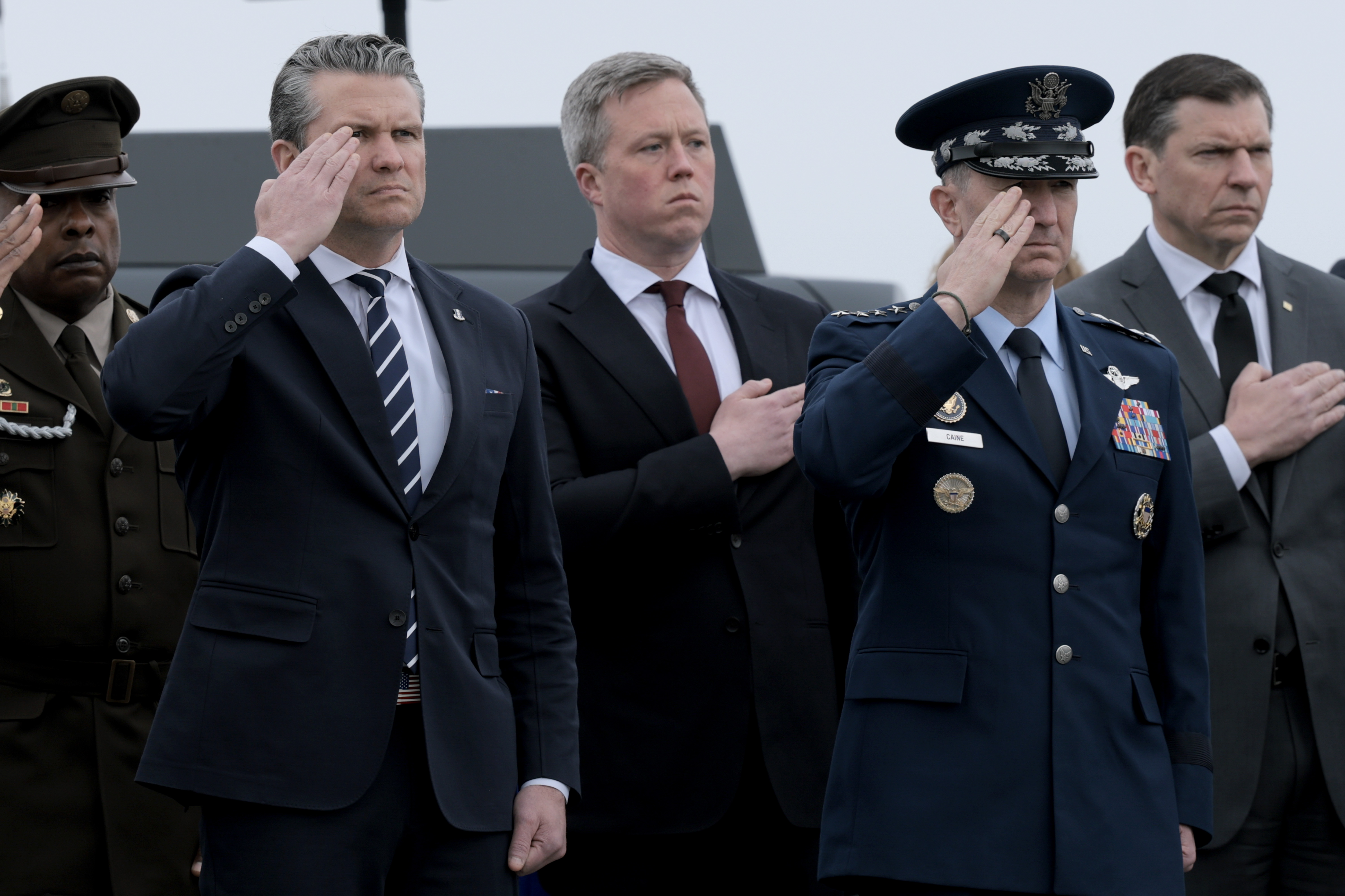 DOVER, DELAWARE - MARCH 07: (L-R) U.S. Secretary of War Pete Hegseth, U.S. Secretary of the Army Daniel Driscoll and Chairman of the Joint Chiefs of Staff Gen. Dan Caine stand at attention as U.S. Army carry teams move flag-draped transfer cases at Dover Air Force Base March 07, 2026 in Dover, Delaware.  Six soldiers from the 103rd Sustainment Command were killed in action by an Iranian drone strike on March 1 in Port Shuaiba, Kuwait during