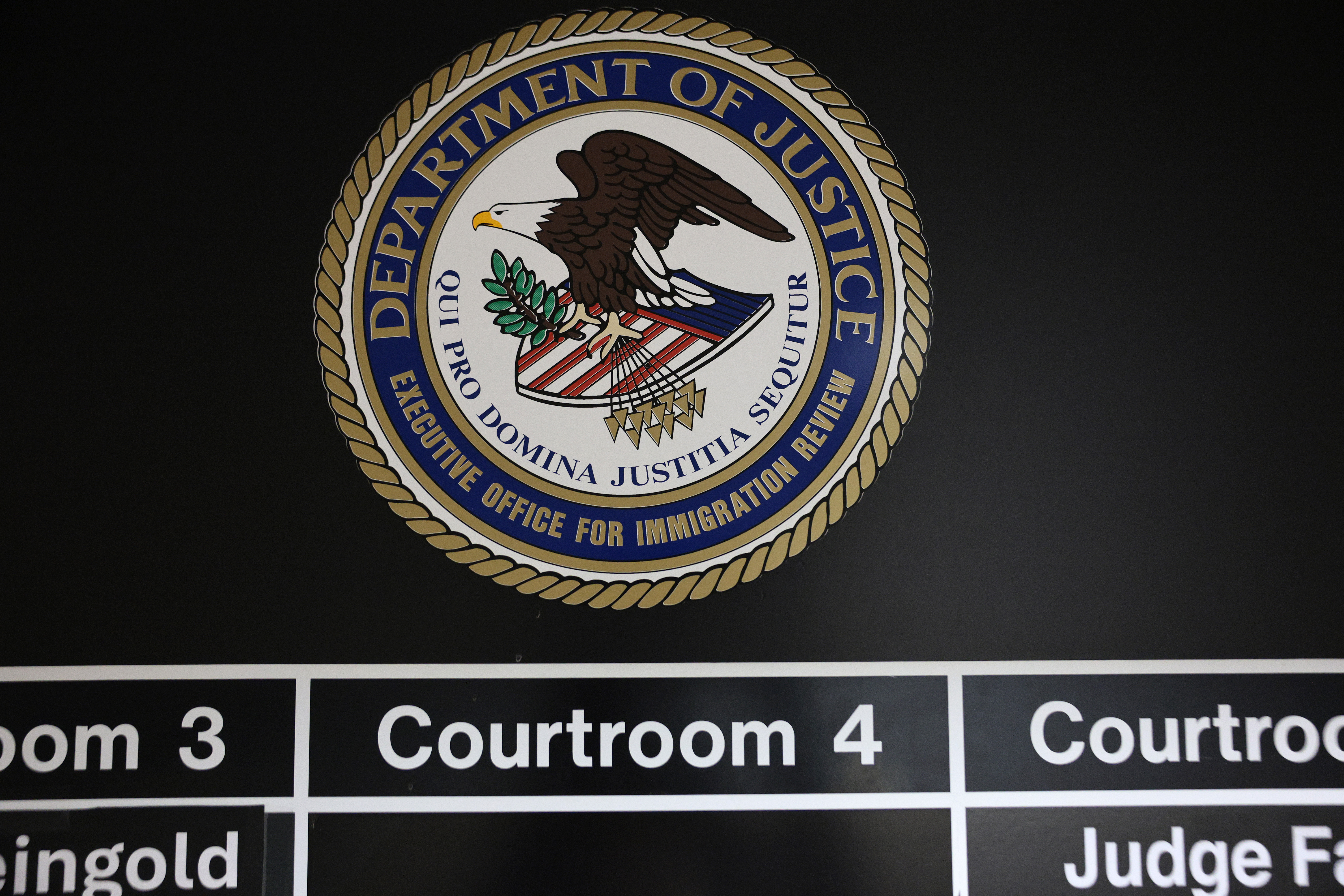 NEW YORK, NEW YORK - JULY 31: A Department of Justice logo is posted outside immigration courts at the Jacob K. Javits Federal Building on July 31, 2026 in New York City. More than 1,400 migrant children across New York, including more than 700 in New York City, are set to lose legal representation as a $200 million federal contract with the Acacia Center for Justice expires. The nonprofit oversees legal services for unaccompanied migrant children and estimates the funding loss will affect more than 24,000 children nationwide. (Photo by Michael M. Santiago/Getty Images)