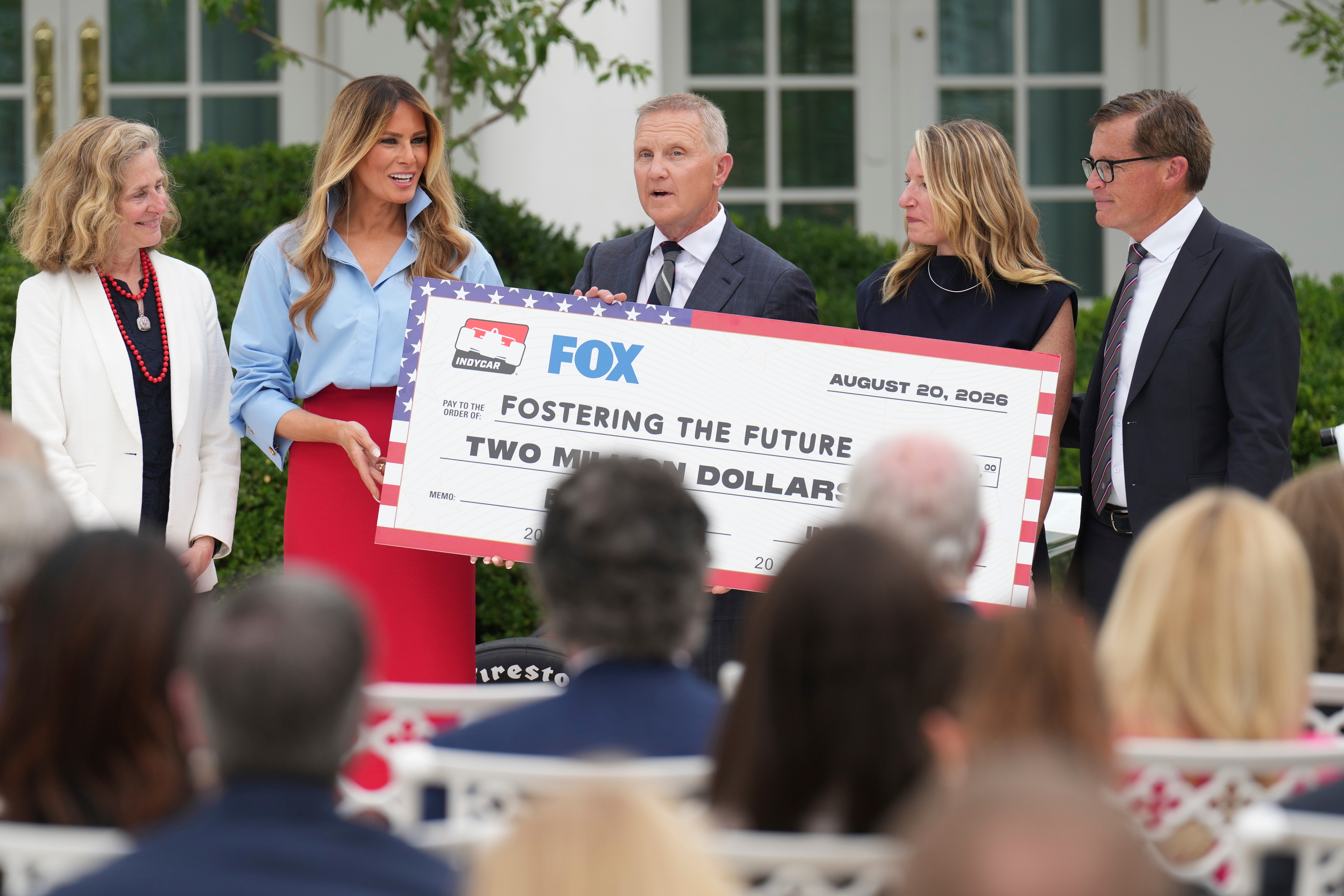 Fox Sports CEO Eric Shanks, center, and IndyCar President Doug Boles, right, present a commemorative check to first lady Melania Trump, second left, to fund her scholarship initiative