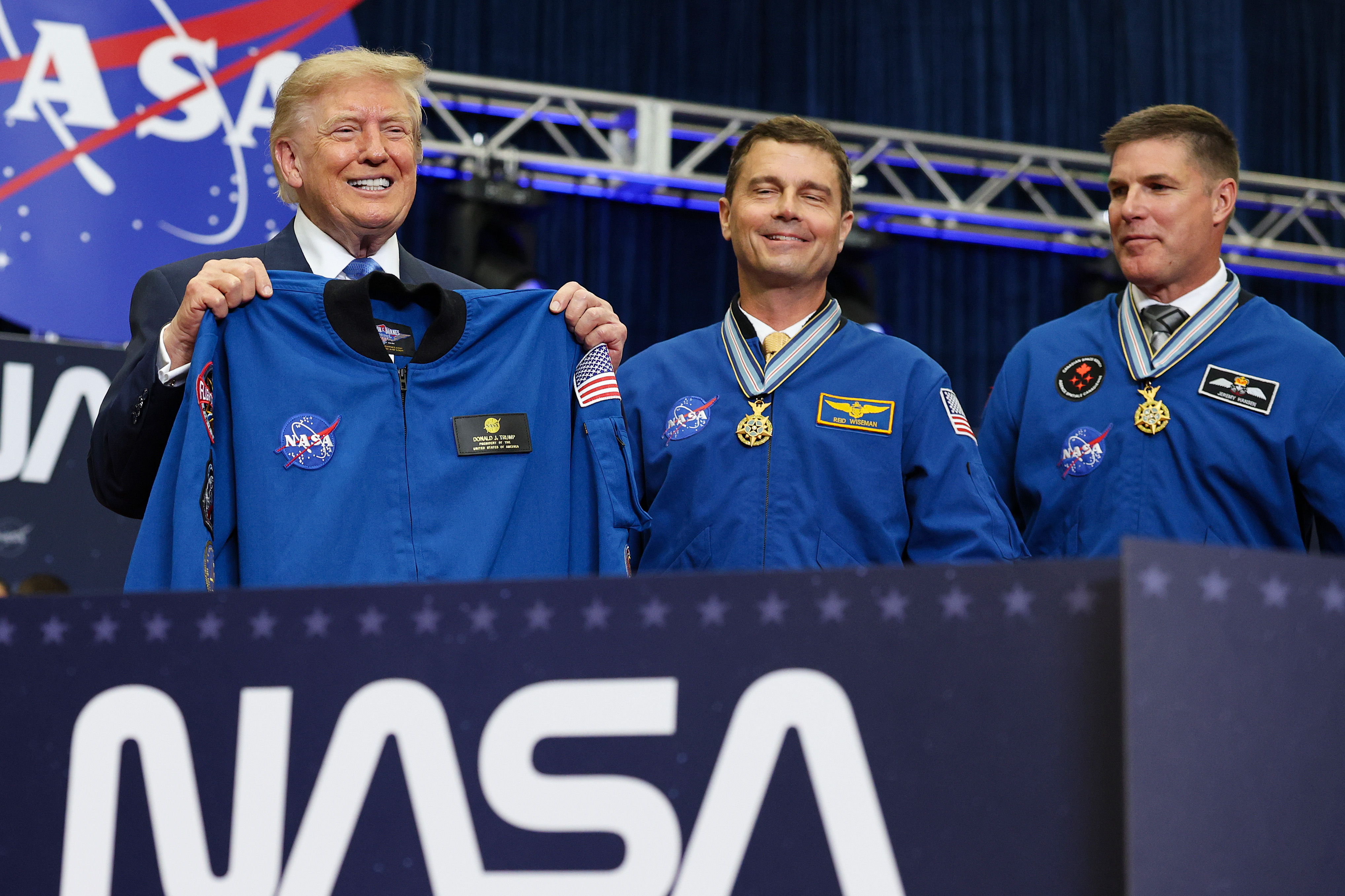 HOUSTON, TEXAS - AUGUST 28: U.S. President Donald Trump (L) holds up a flight jacket gifted to him by the Artemis II crew alongside commander Reid Wiseman (C) and mission specialist Jeremy Hansen of CSA (Canadian Space Agency) during a ceremony honoring the Artemis II crew members at NASA's Johnson Space Center on August 28, 2026 in Houston, Texas. Artemis II crew members, NASA astronauts Reid Wiseman, Victor Glover, and Christina Koch and Canadian astronaut Jeremy Hansen, traveled further into space than any other humans before on the first crewed mission around the moon in more than 50 years. (Photo by Win McNamee/Getty Images)
