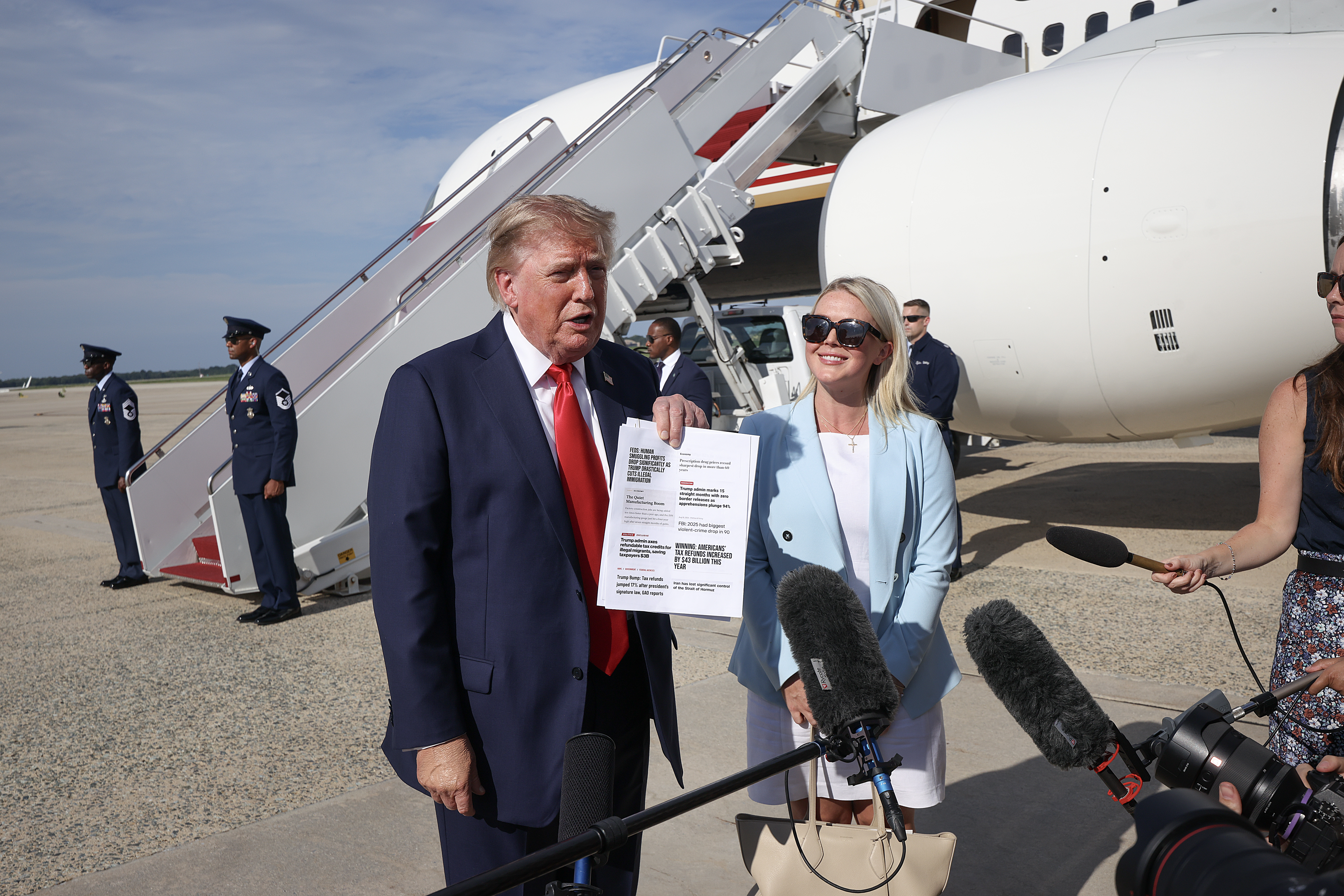 JOINT BASE ANDREWS, MARYLAND - AUGUST 21: U.S. President Donald Trump shows copies of recent headlines as he speaks with reporters with Press Secretary Karoline Leavitt looking on before boarding Air Force One on August 21, 2026 in Joint Base Andrews, Maryland. President Trump is traveling to South Carolina for a campaign rally with Darline Graham. (Photo by Win McNamee/Getty Images)