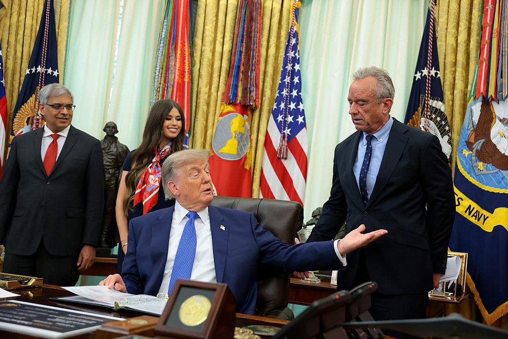 WASHINGTON, DC - AUGUST 10: U.S. President Donald Trump (C) reaches out to shake hands with Health and Human Services Secretary Robert F. Kennedy Jr. before signing an executive order calling for childhood vaccine shots to be spaced out into separate visits during an event in the Oval Office of the White House on August 10, 2026 in Washington, DC. During his second term, Trump has urged Health and Human Services Secretary Robert F. Kennedy Jr. to investigate further research on vaccines. Also pictured is National Institutes of Health Director Jay Bhattacharya (L), and Jayme Leagh Franklin with the The Conservateur (2nd-L). (Photo by Anna Moneymaker/Getty Images)