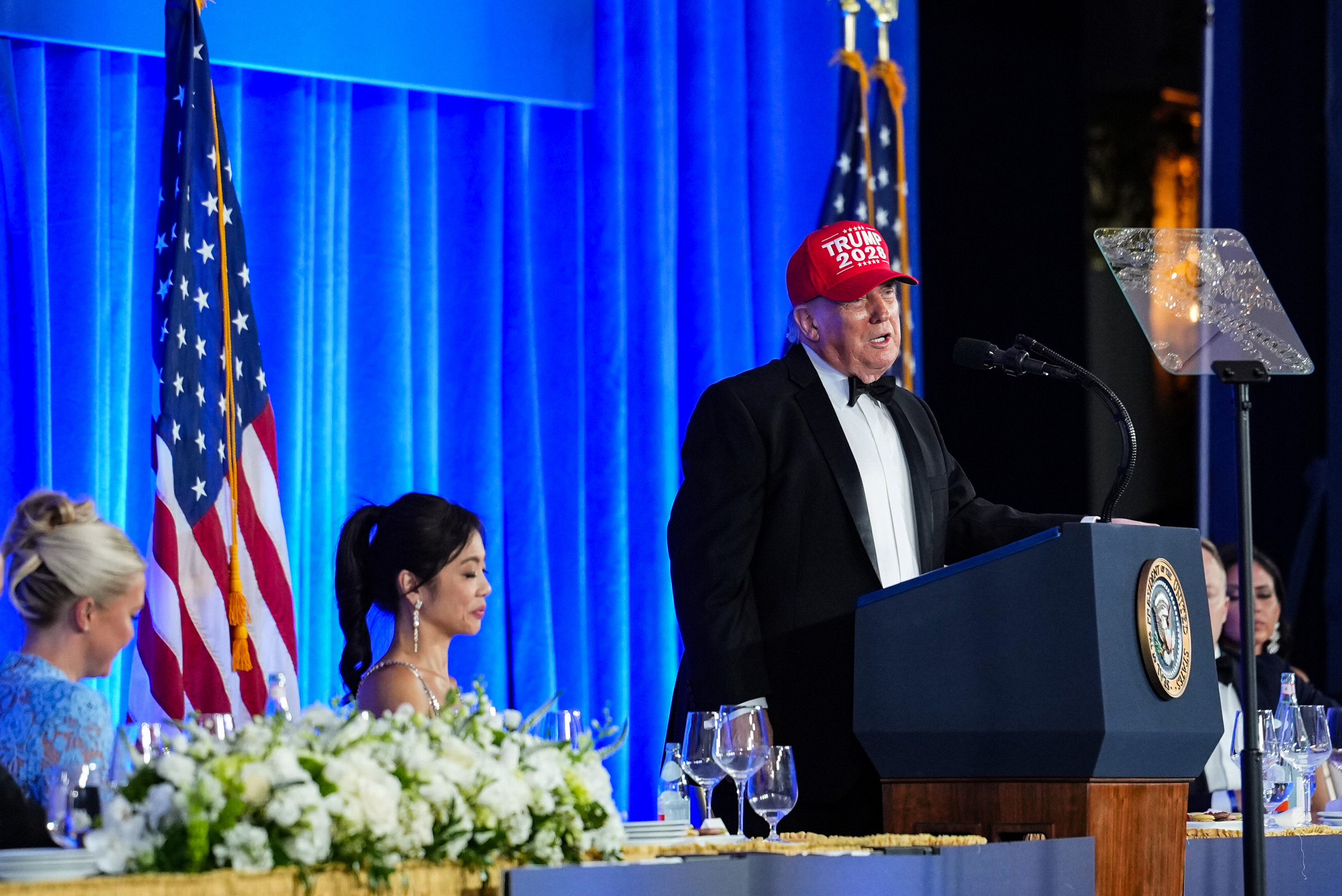 WASHINGTON, DC - JULY 24: U.S. President Donald Trump puts on a TRUMP 2028 hat while speaking during the re-scheduled White House Correspondents Dinner in the Presidential Ballroom at the Waldorf Astoria on July 24, 2026 in Washington, DC. The annual gala hosted by the White House Correspondents Association was re-scheduled to tonight after the original event in April was cut short when an armed man, later identified as Cole Tomas Allen, attempted to get past a Secret Service checkpoint. (Photo by Eric Lee/Getty Images)