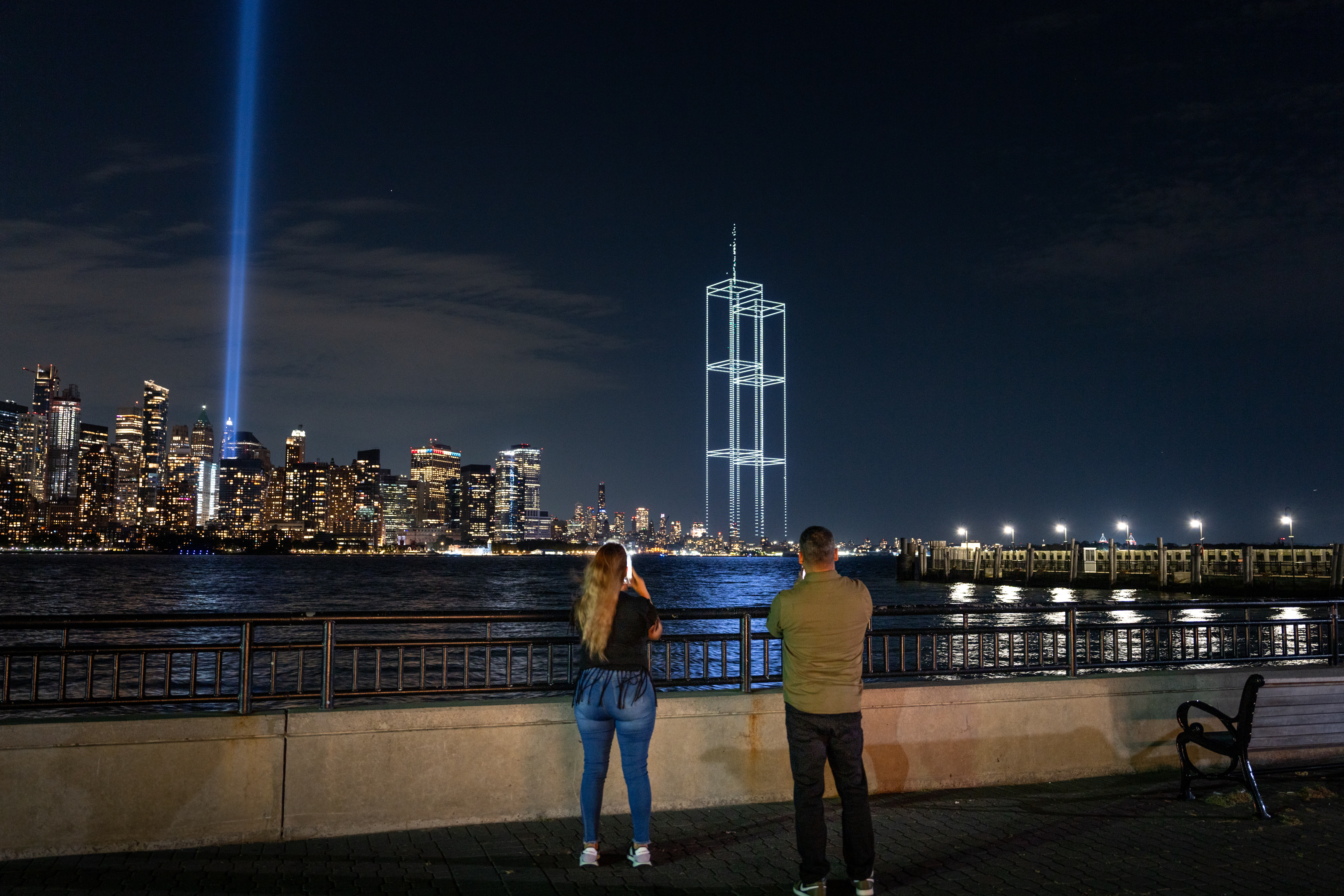 JERSEY CITY, NEW JERSEY - SEPTEMBER 9: People watch and take pictures as a drone light show depicting the twin towers appears in the skyline  during testing of Tribute in Light installation in lower Manhattan on September 9, 2026, as seen from Liberty State Park in Jersey City, New Jersey. The twin beams shine from dusk on September 11 until dawn on September 12 every year. (Photo by Jeremy Weine/Getty Images)
