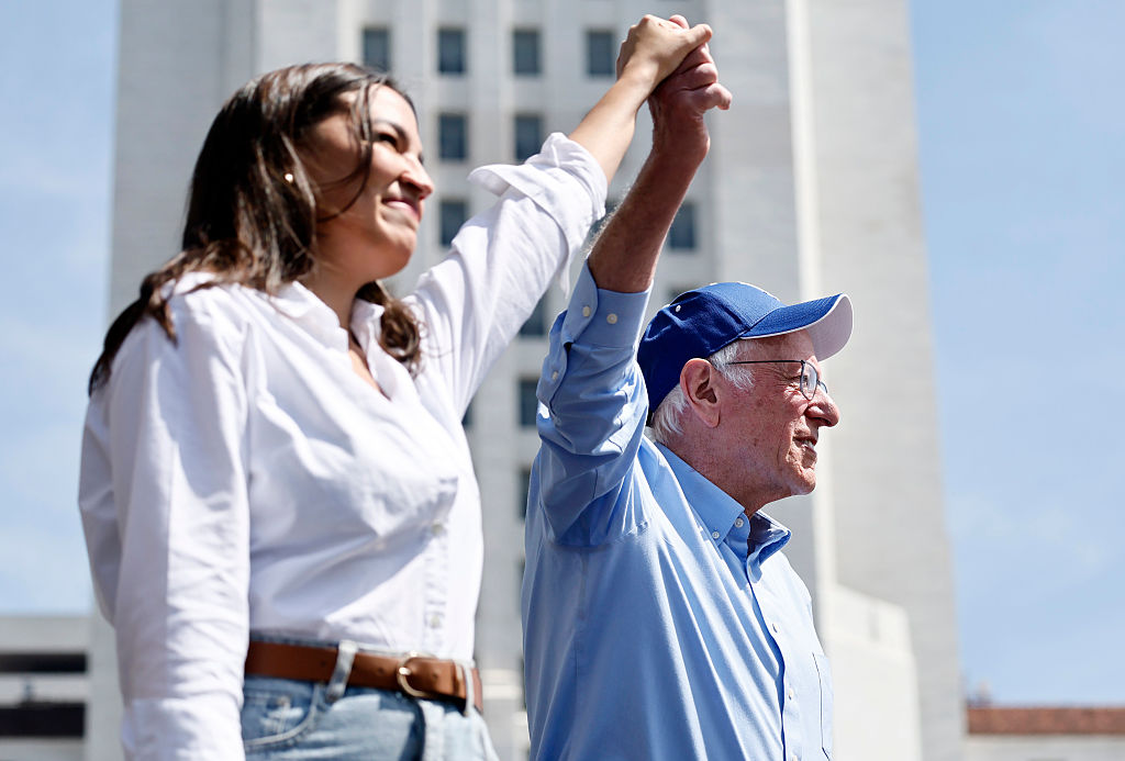 LOS ANGELES, CALIFORNIA - APRIL 12: U.S. Sen. Bernie Sanders (I-VT) and Rep. Alexandria Ocasio-Cortez (D-NY) hold hands during a stop on their ‘Fighting Oligarchy’ tour at Grand Park on April 12, 2025 in Los Angeles, California. An estimated 36,000 people attended the rally which also saw Neil Young and Joan Baez perform.   (Photo by Mario Tama/Getty Images)