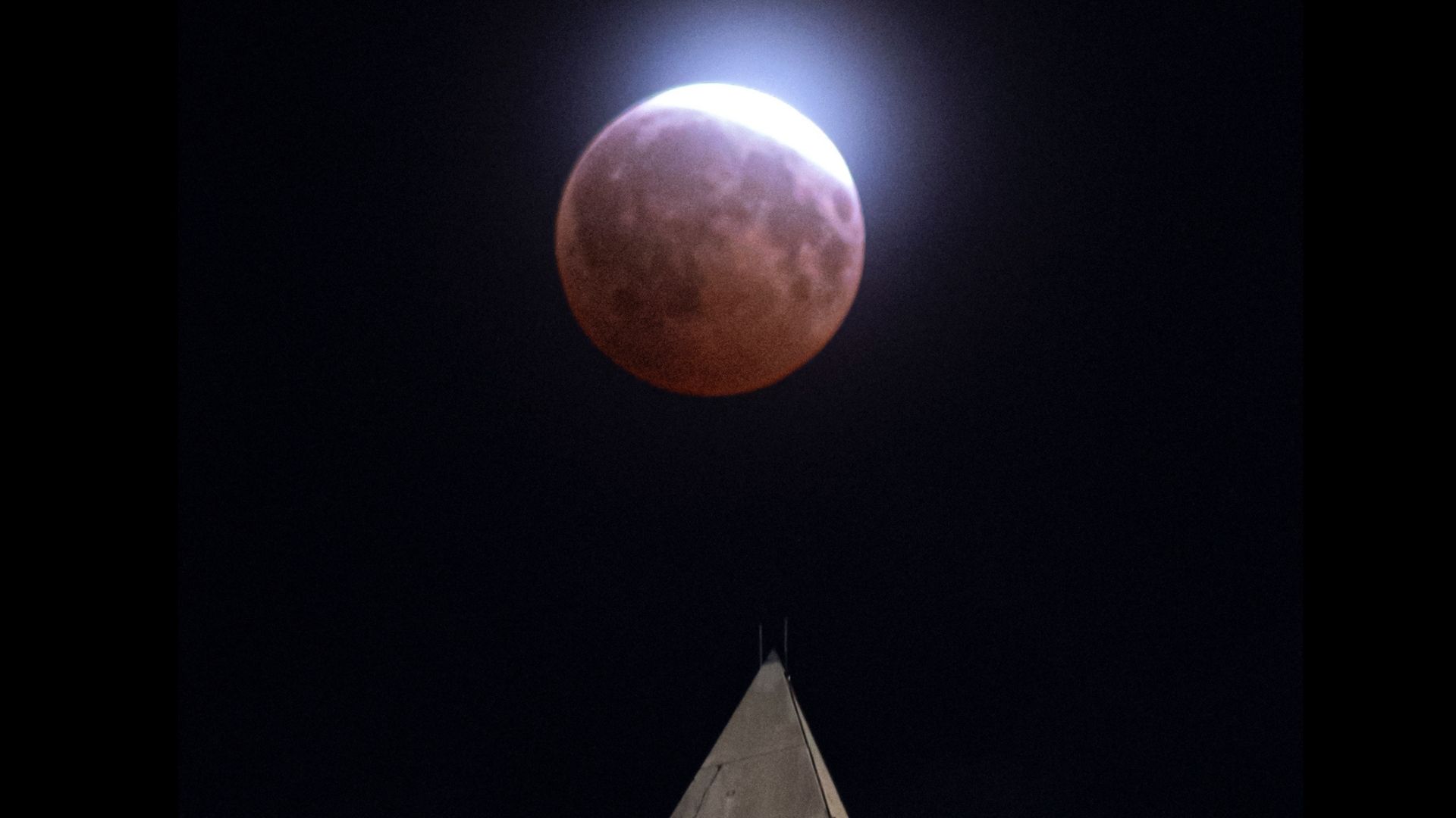 A lunar eclipse of the moon is seen through light clouds above the Washington Monument in Washington, Thursday, Aug. 27, 2026. (AP Photo/Cliff Owen)