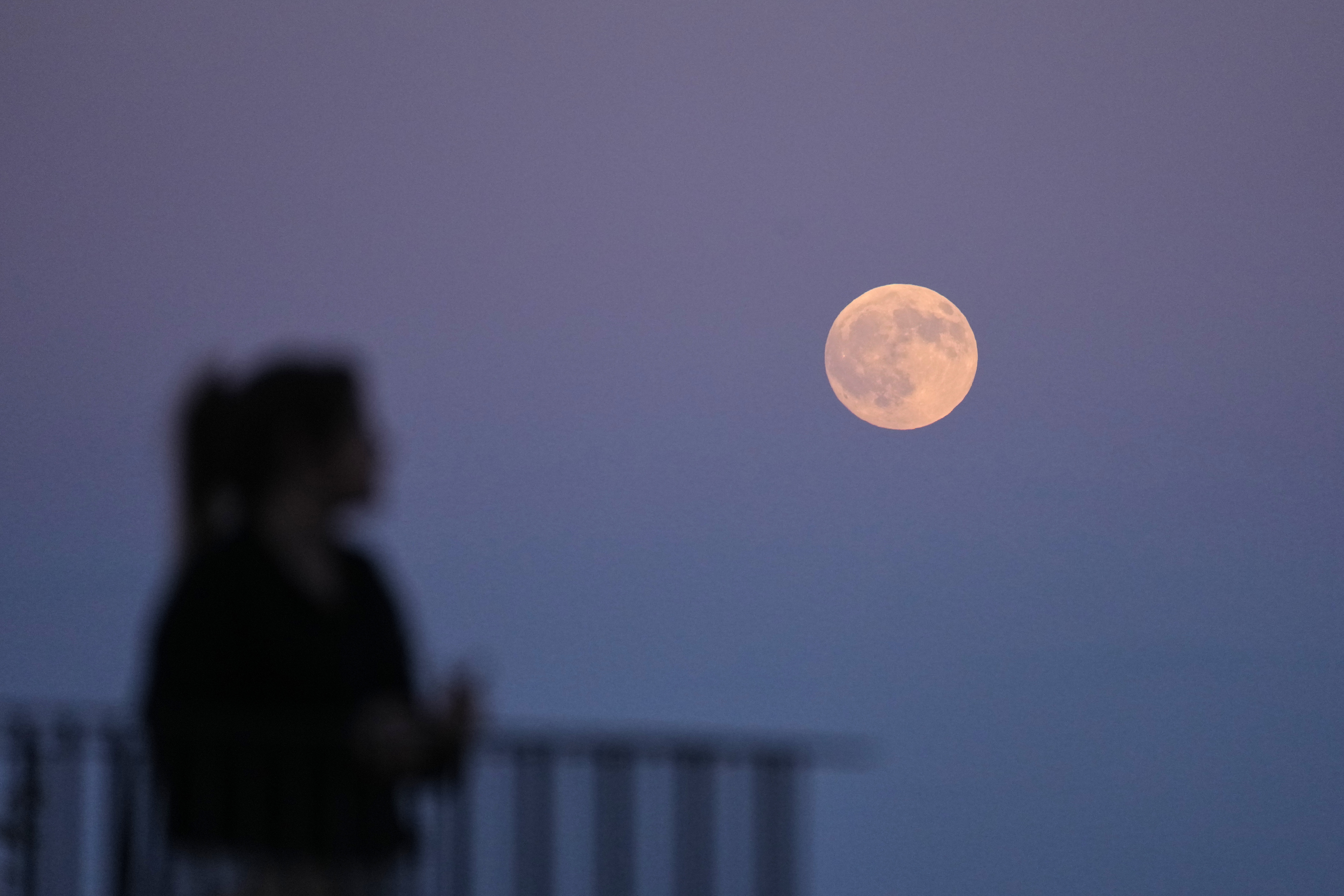 A person watches as the full moon rises above the Tagus river hours before a lunar eclipse in Lisbon, Thursday, Aug. 27, 2026. (AP Photo/Armando Franca)