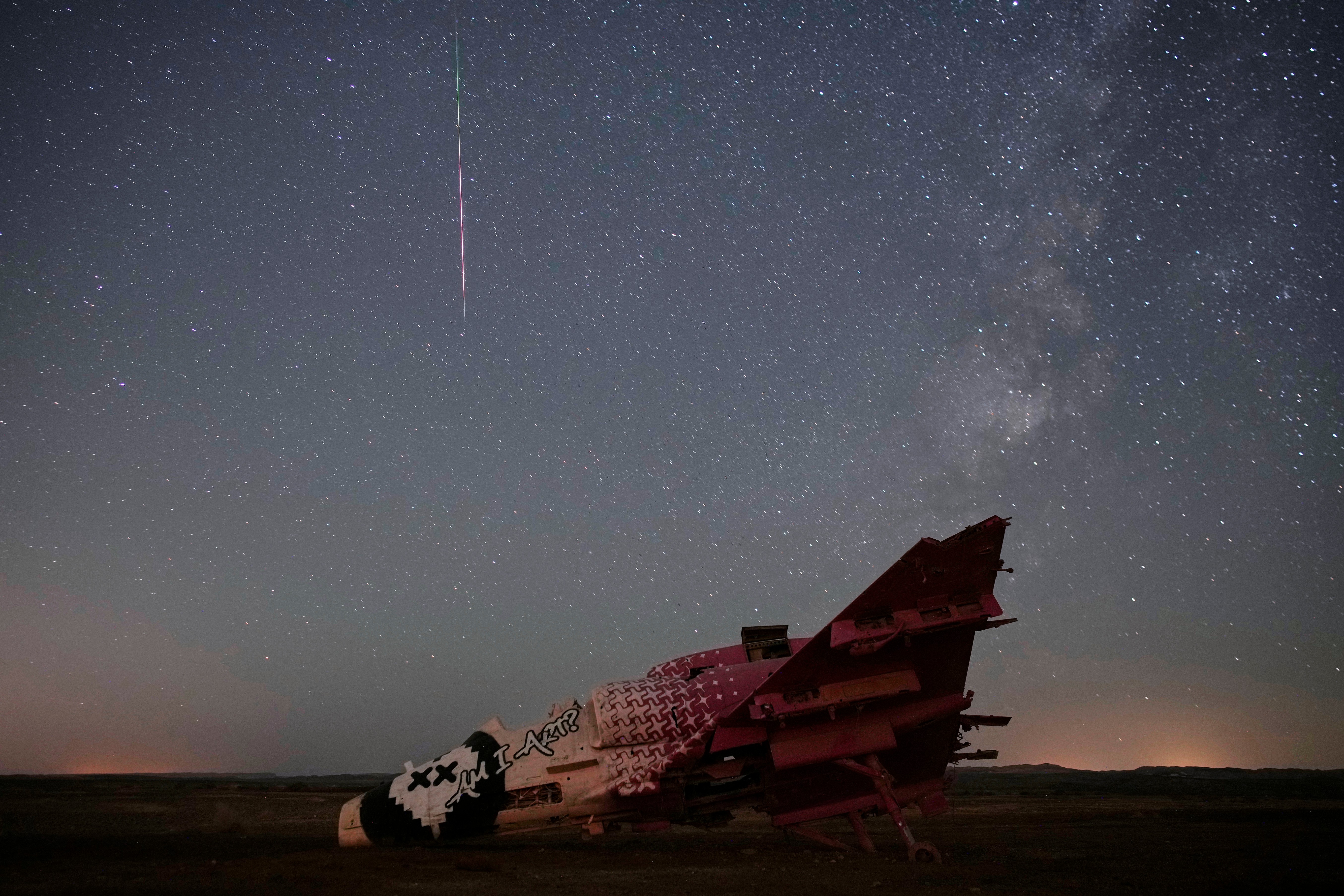 A meteor streaks above a destroyed aircraft used for training purposes in the Negev Desert, Israel, Aug. 13, 2026. (Image Source: AP/Ohad Zwigenberg)
